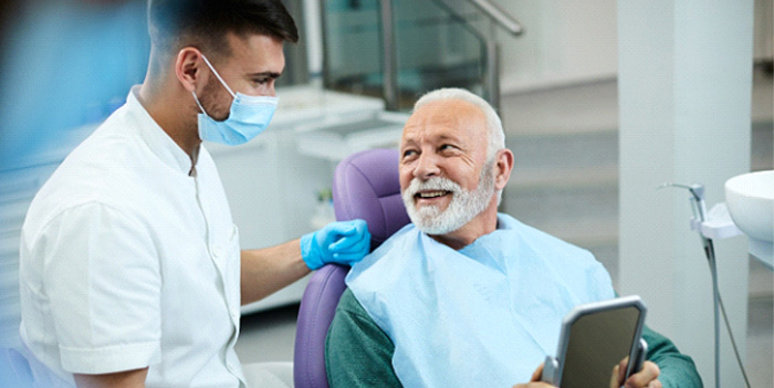 Senior patient looking at dentist while holding small mirror