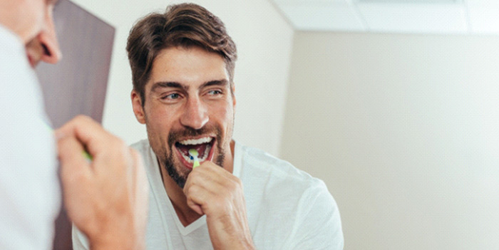 Man smiling while brushing his teeth