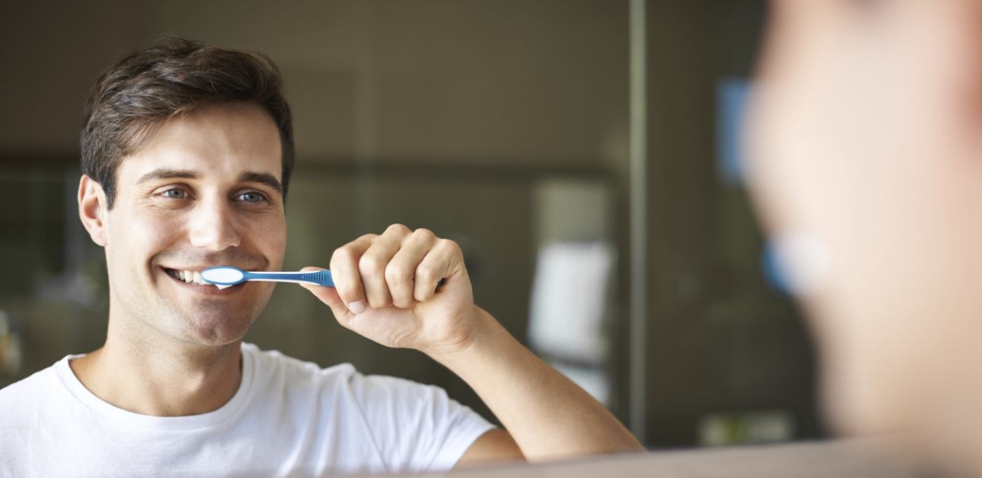 Man smiling while brushing his teeth  