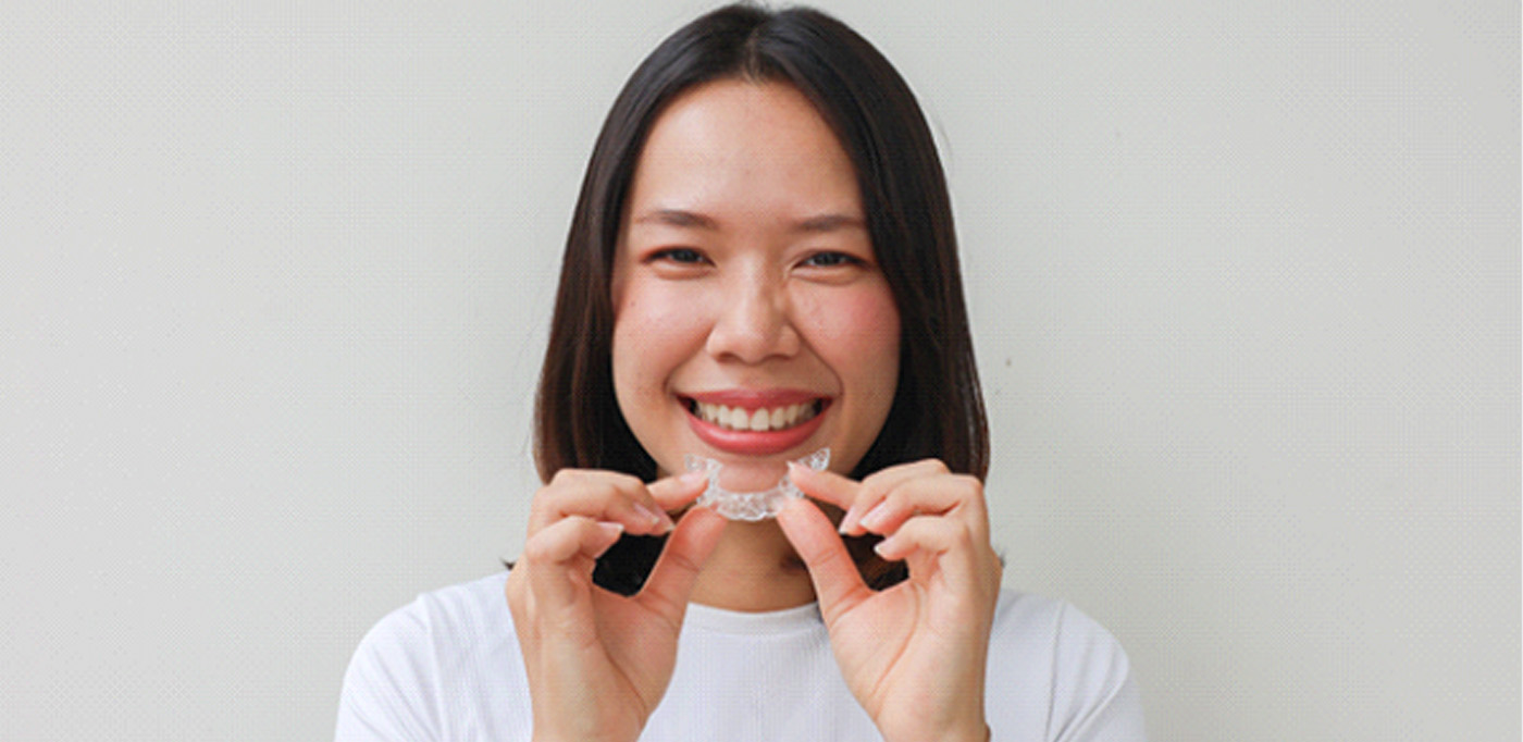 Woman smiling while holding clear aligner