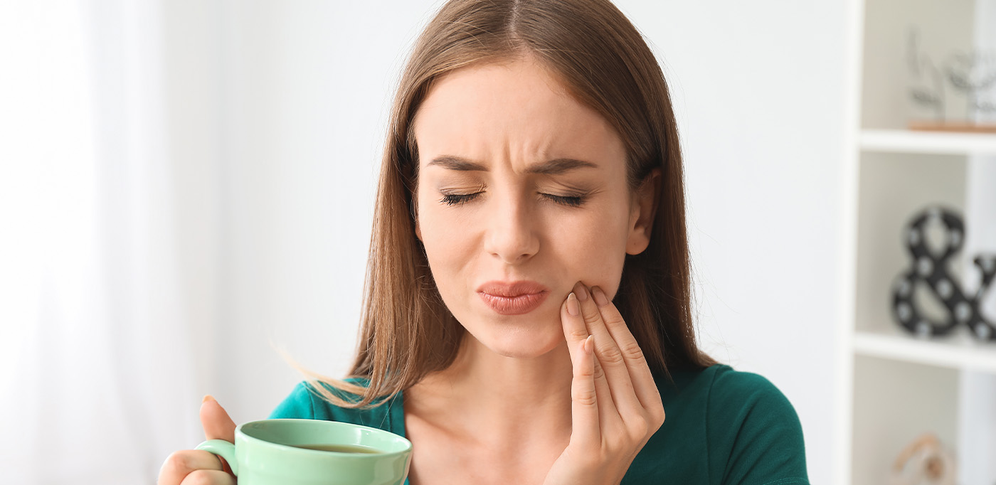 Woman holding her aching tooth after sipping coffee