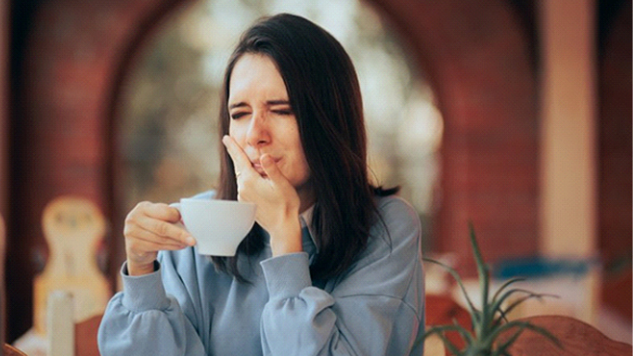 Woman holding her aching tooth after sipping coffee